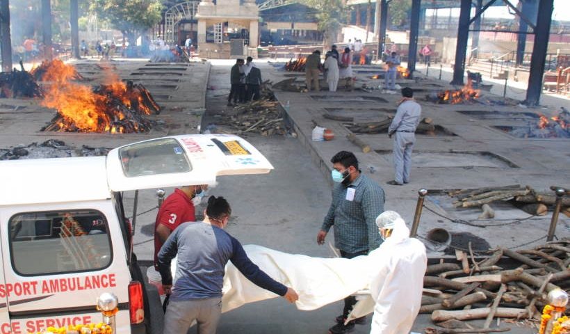 स्वास्थ्य कार्यकर्ता और रिश्तेदार अंतिम संस्कार के लिए कोविड -19 प्रभावित पीड़ितों के शव को ले जाते