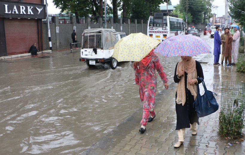 Women shield themselves with umbrellas as they walk past an inundated street during rains