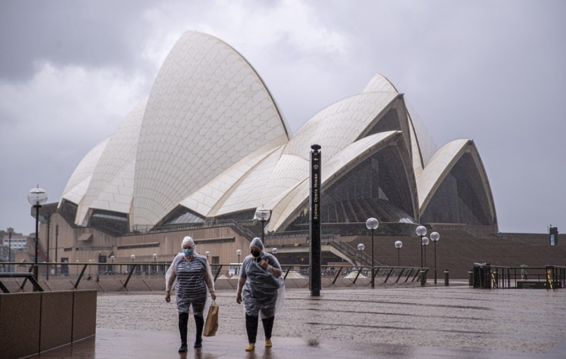 People wearing face masks walk past the Sydney Opera House in Sydney, Australia.