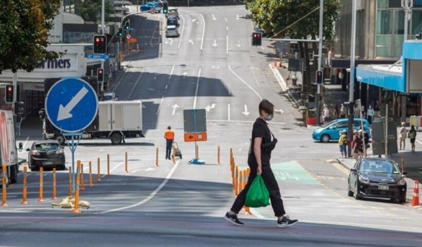 A woman wearing a face mask walks across a street in Auckland, New Zealand