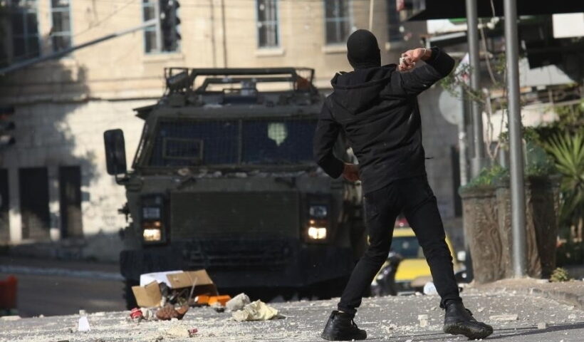 A Palestinian protester hurls a stone at an Israeli military vehicle during clashes in the West Bank city of Nablus,