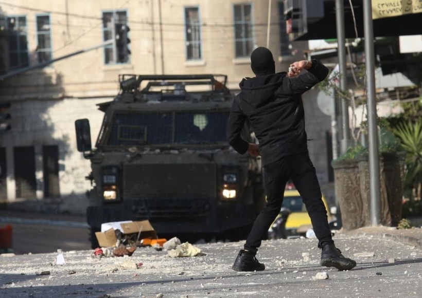 A Palestinian protester hurls a stone at an Israeli military vehicle during clashes in the West Bank city of Nablus,
