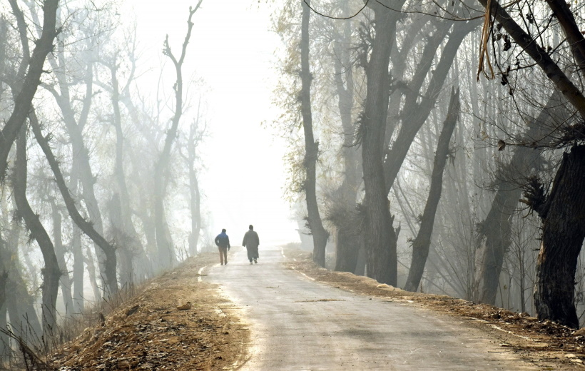 Srinagar: People walk past on a road during dense fog on a cold morning in Srinagar on Sunday,