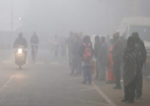 New Delhi: People stand on a road waiting for a bus as the thick layer of fog engulfs on a cold morning, in New Delhi on Monday