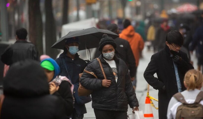 People wearing face masks walk along Fulton Street in New York, the United States,