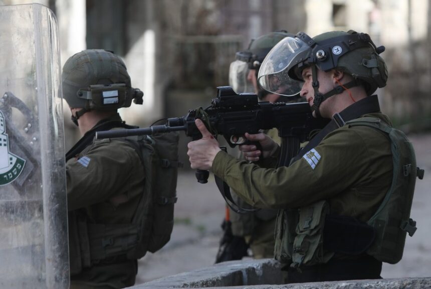 An Israeli soldier aims his gun at Palestinian protesters during clashes in the West Bank city of Hebron, on March 1, 2022