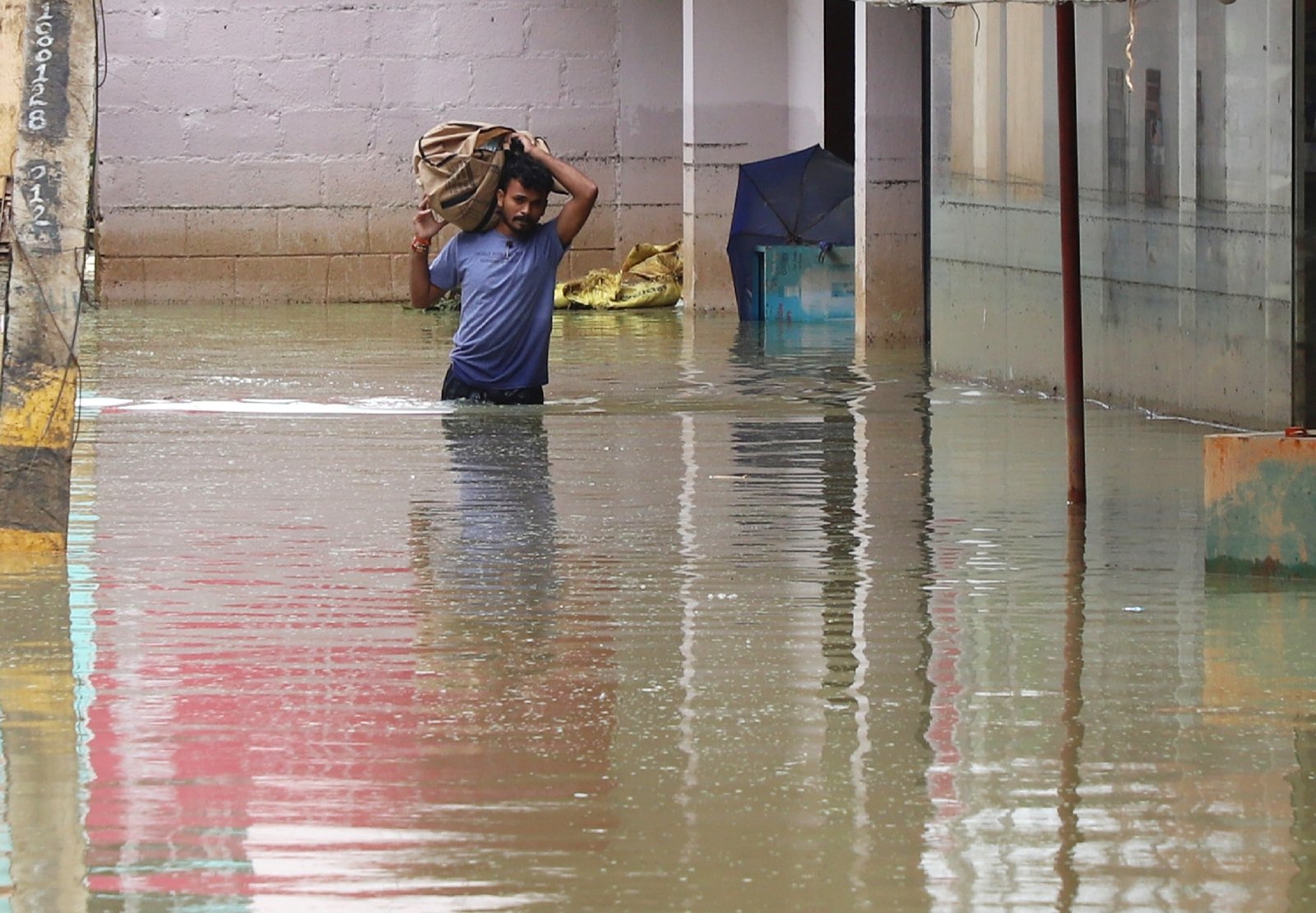 A man with his belongings crosses a flooded road at Sarjapur