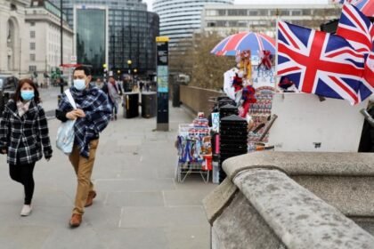 People wearing masks walk on a street in London
