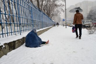 A displaced person begs on a snow-covered road