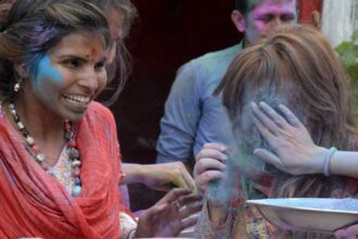 A Pakistani Hindu scatters color powder on a woman's face