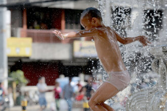 A boy frolics at a fountain to cool off from the summer heat