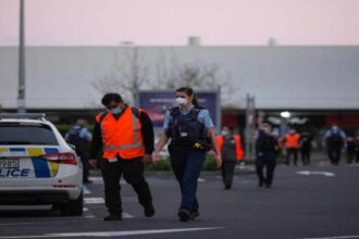 Police officers stand guard near the New Lynn supermarket in Auckland, New Zealand